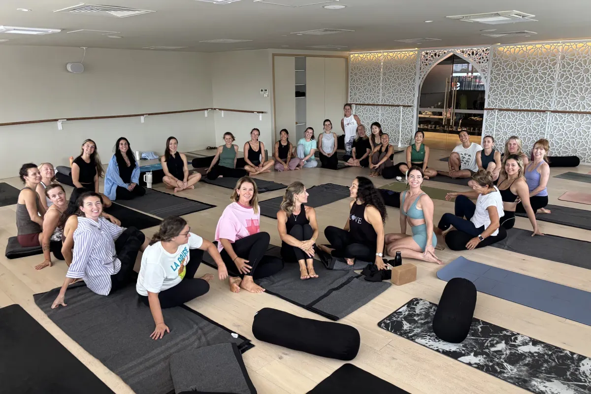 A big class sitting on their mats and smiling in the bright, open Flolo Mermaid Beach studio